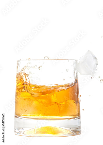 glass of whiskey with ice cubes splashing out over white