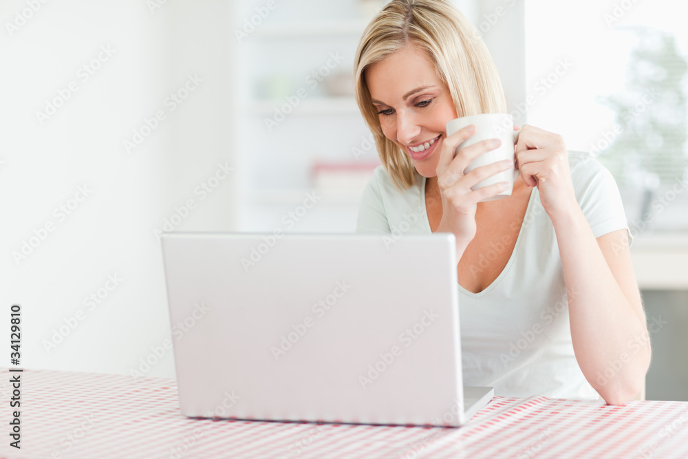 Close up of a woman holding coffee looking at the laptop in fron