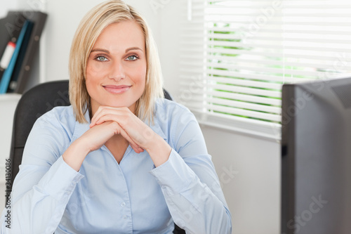 Cute blonde woman with chin on her hands behind a desk