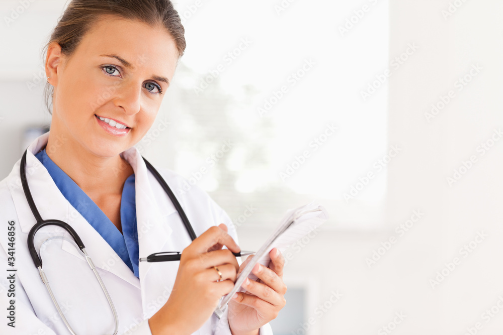 Close up of a smiling brunette doctor writing something down loo Close up of a smiling brunette doctor writing something down loo