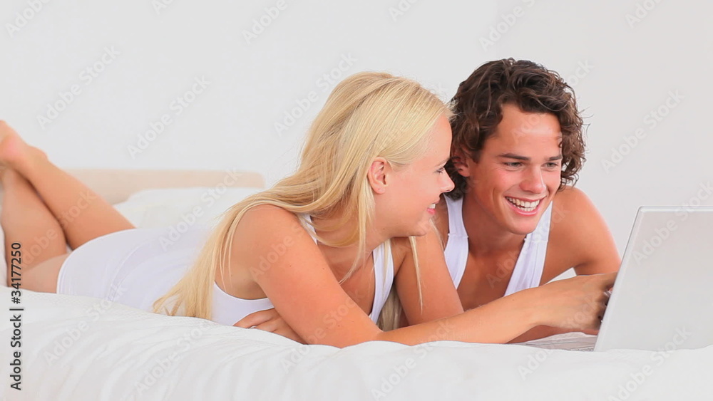 Joyful couple with a laptop lying in their bed Joyful couple with a laptop lying in their bed