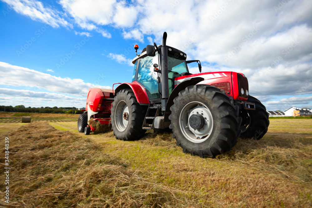 Naklejka premium tractor collecting haystack in the field