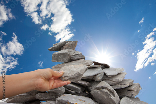 Woman adds rock to cairn under sun filled sky