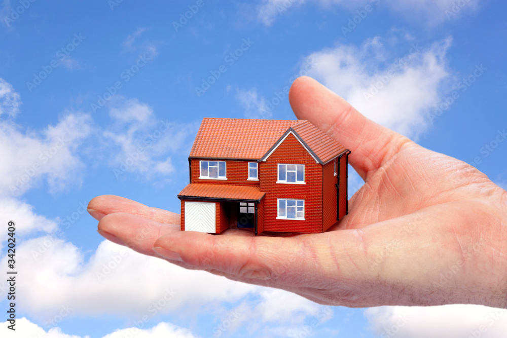 Hand holding a model home against sky background. Hand holding a model home against sky background.