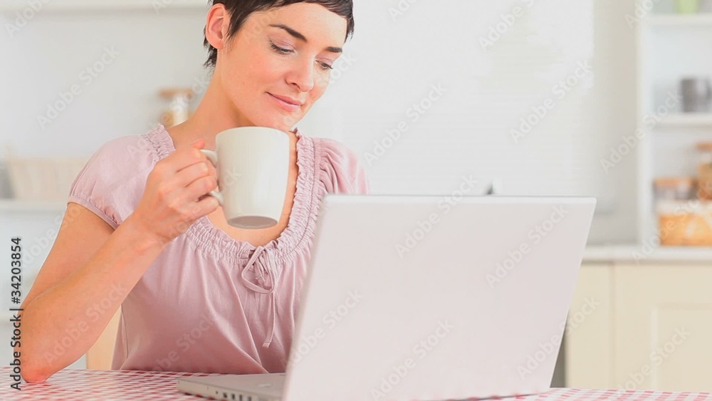 Lovely woman drinking tea while using her laptop Lovely woman drinking tea while using her laptop