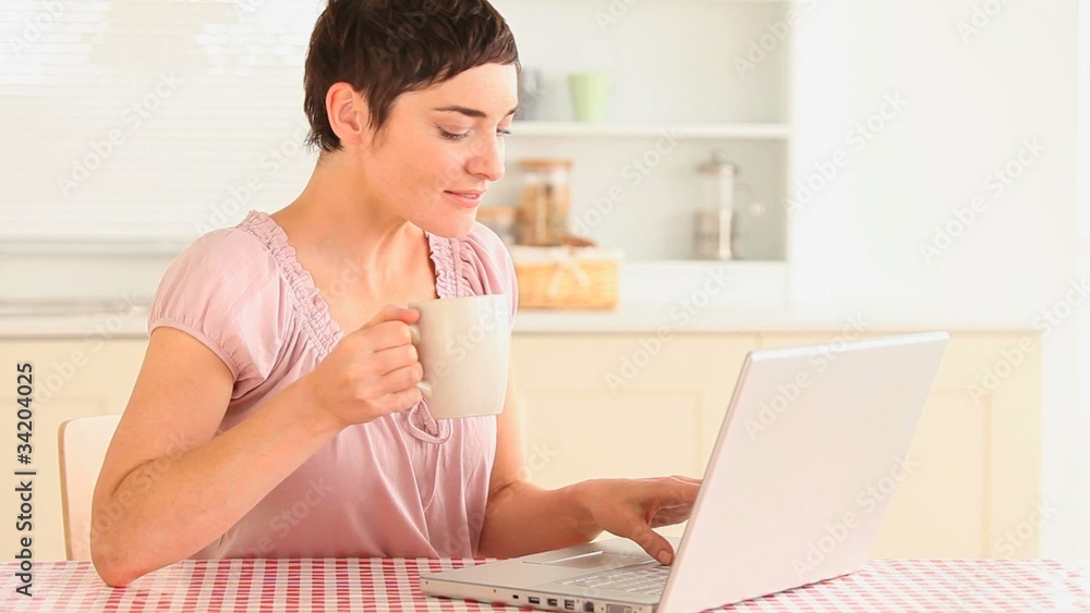 Woman drinking coffee while using a laptop Woman drinking coffee while using a laptop