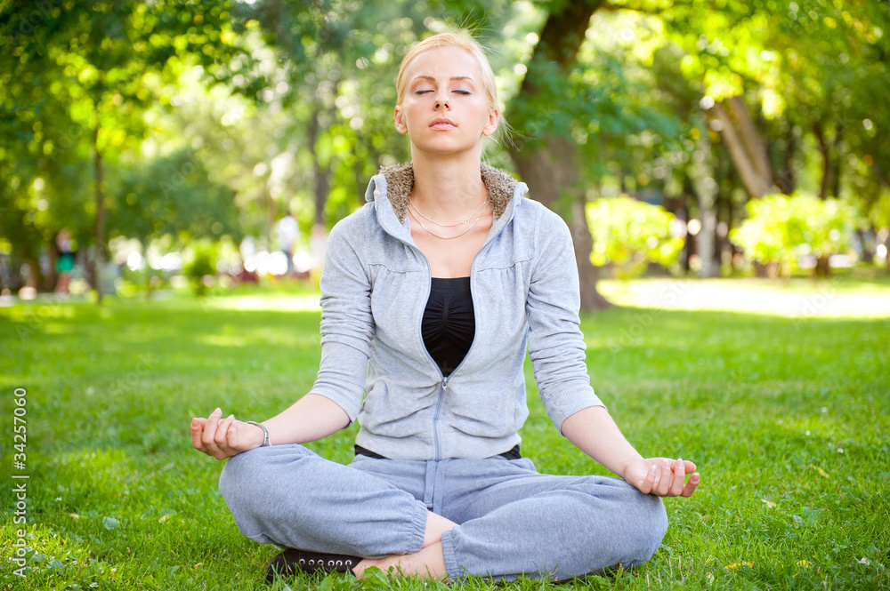 Portrait of young woman meditating in pose of lotus on green gra Portrait of young woman meditating in pose of lotus on green gra