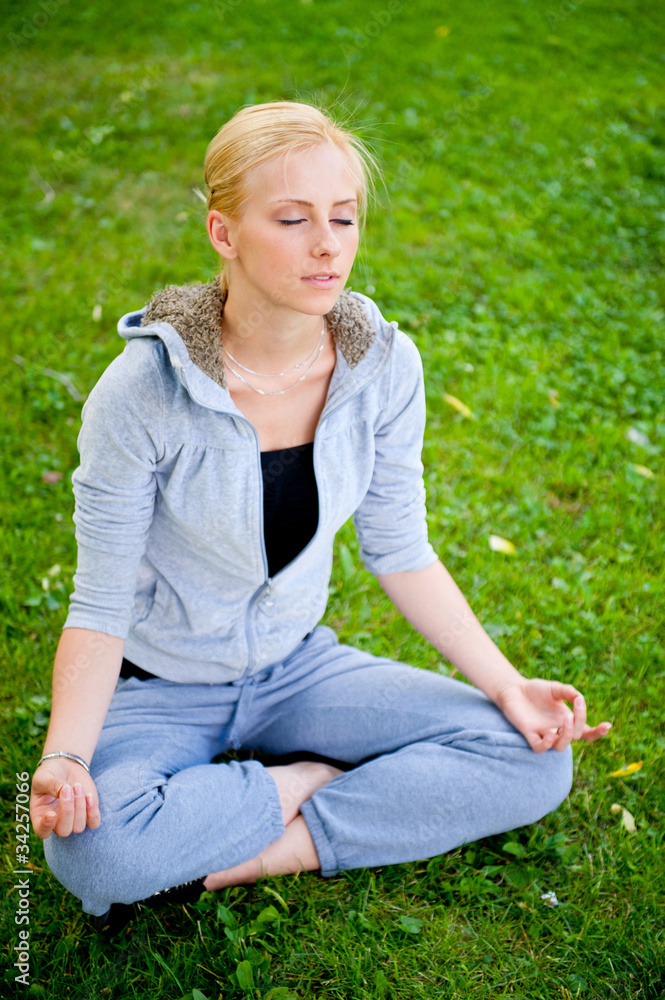 Portrait of young woman meditating in pose of lotus on green gra Portrait of young woman meditating in pose of lotus on green gra