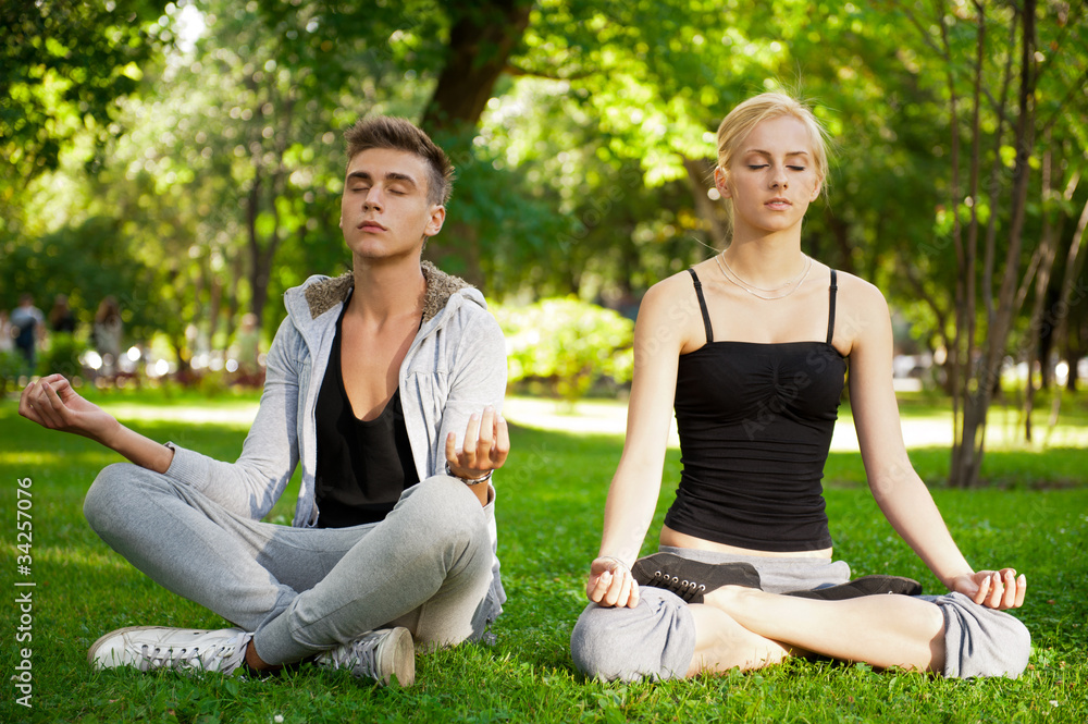 Portrait of young beautiful couple sitting in lotus pose on gree Portrait of young beautiful couple sitting in lotus pose on gree
