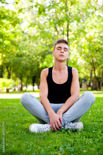 Beautiful young man in meditation pose outdoors. © Milles Studio