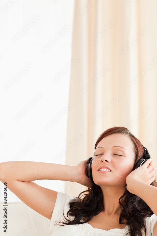 Naklejka premium Red-haired woman relaxing on a sofa listening to music
