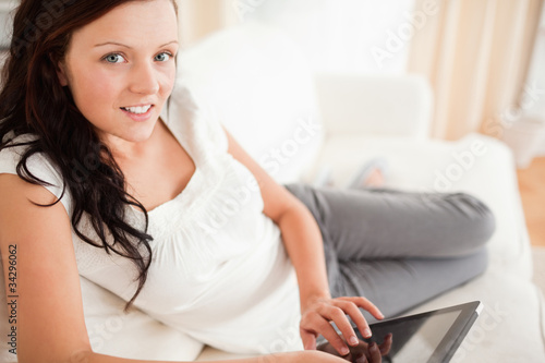 Cute red-haired woman lying on a sofa with a tablet looking into