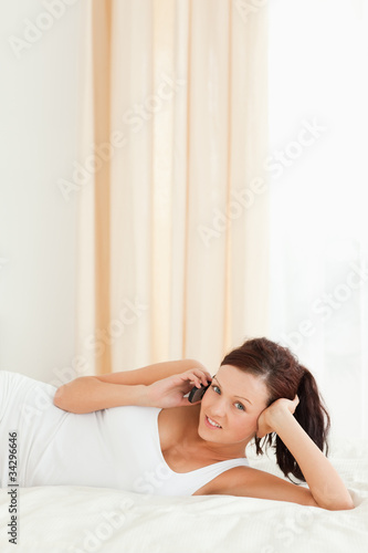 Red-haired Woman phoning on a bed looking into the camera