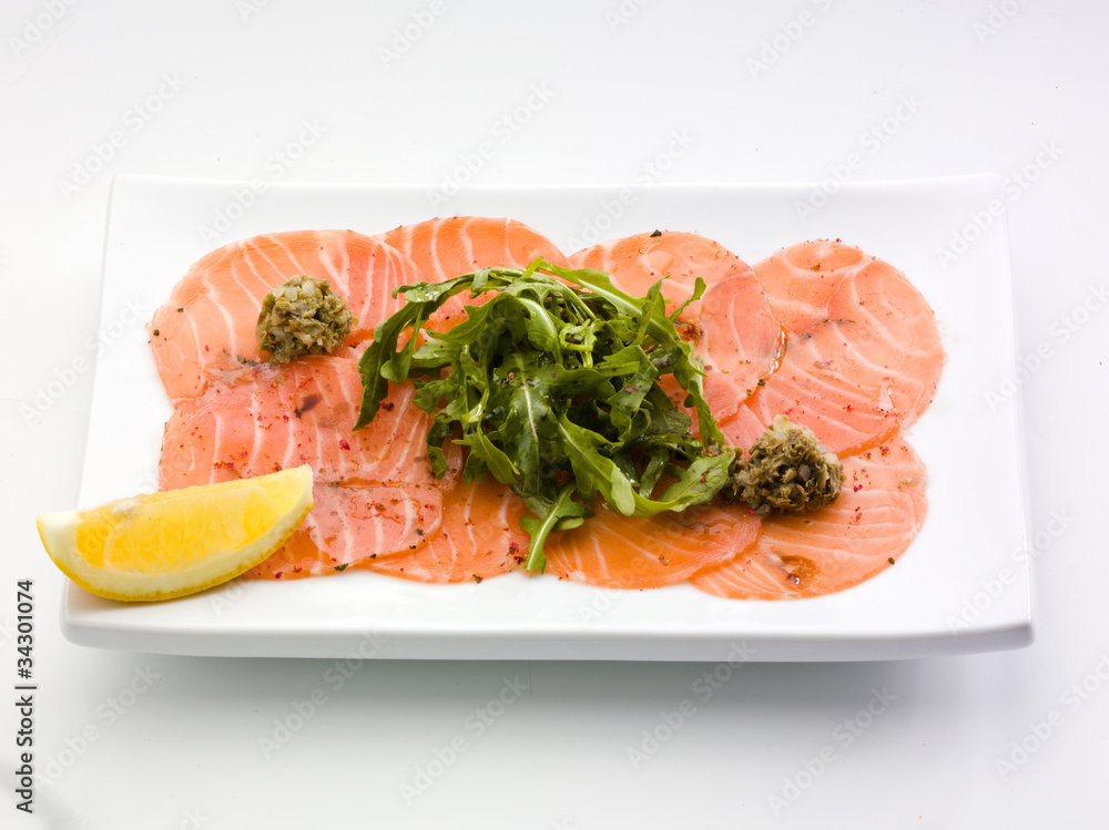 Salmon carpaccio in a white plate with salad
