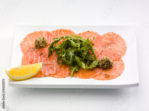 Salmon carpaccio in a white plate with salad