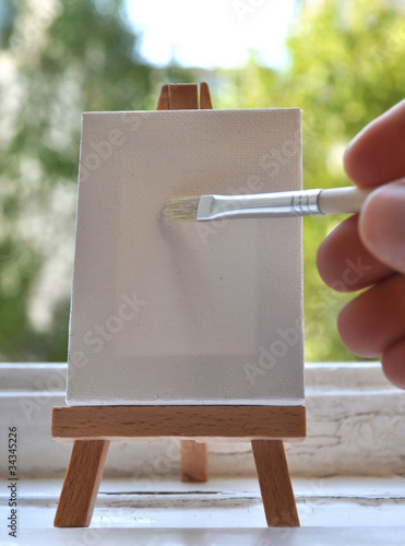 Hand mit Pinsel vor Staffelei mit Leinwand