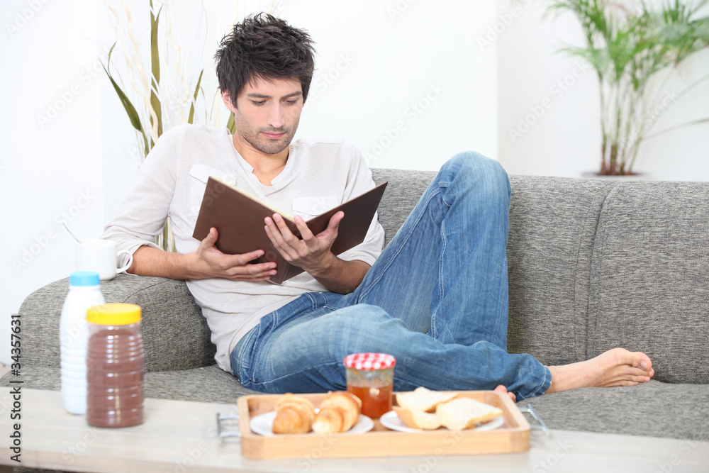 Man reading and having breakfast on a sofa Man reading and having breakfast on a sofa
