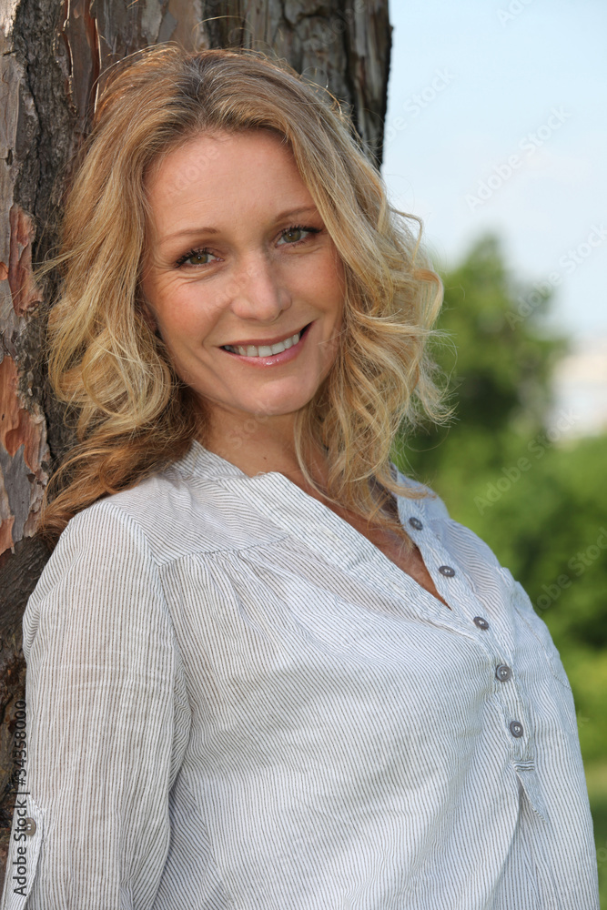 Smiling woman leaning against rough barked tree Smiling woman leaning against rough barked tree