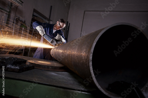 Worker cutting pipe with angel grinder.