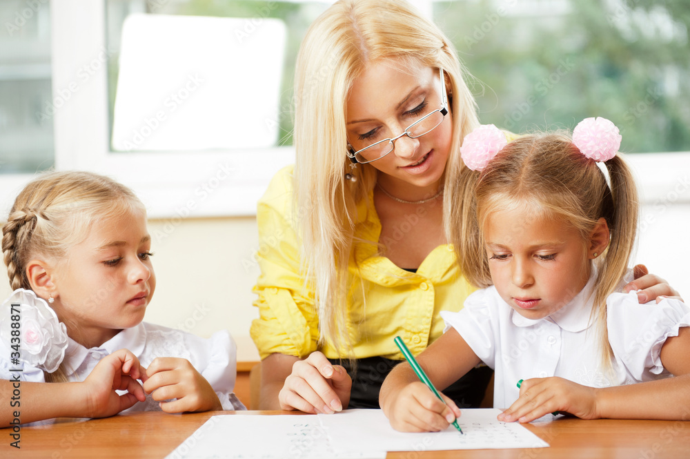 Teacher helps to little girls to make an exercises in classroom Teacher helps to little girls to make an exercises in classroom