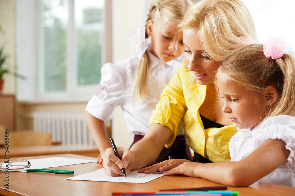 Young pretty teacher helping her little students in classroom Young pretty teacher helping her little students in classroom