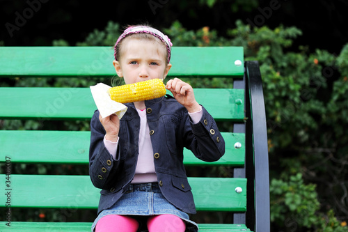 Pretty child girl eating a boiled corn outdoors