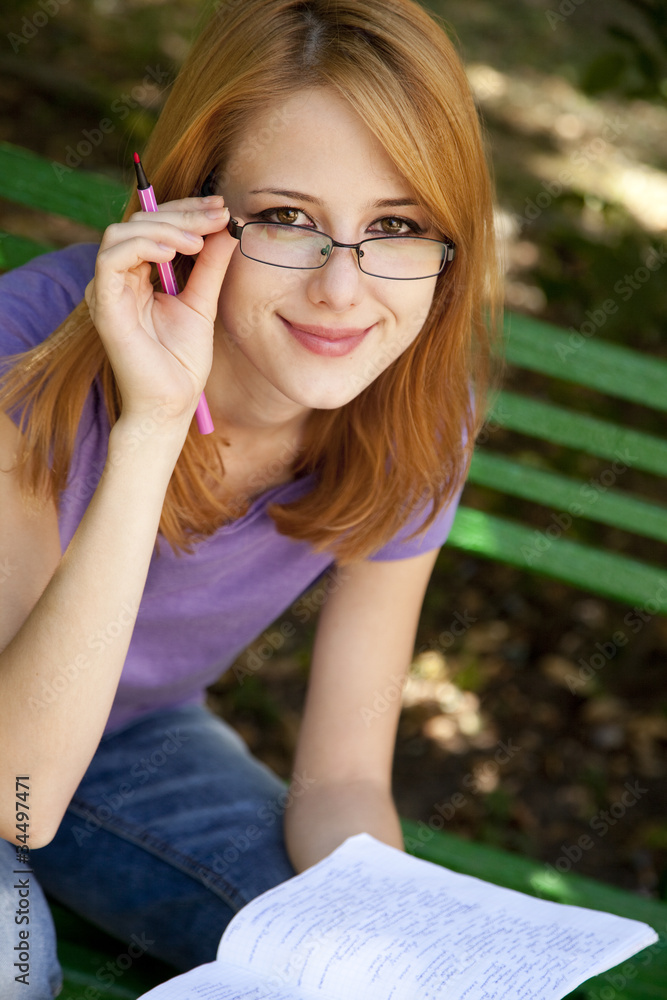Obraz premium Redhead girl in glasses doing homework at the park.