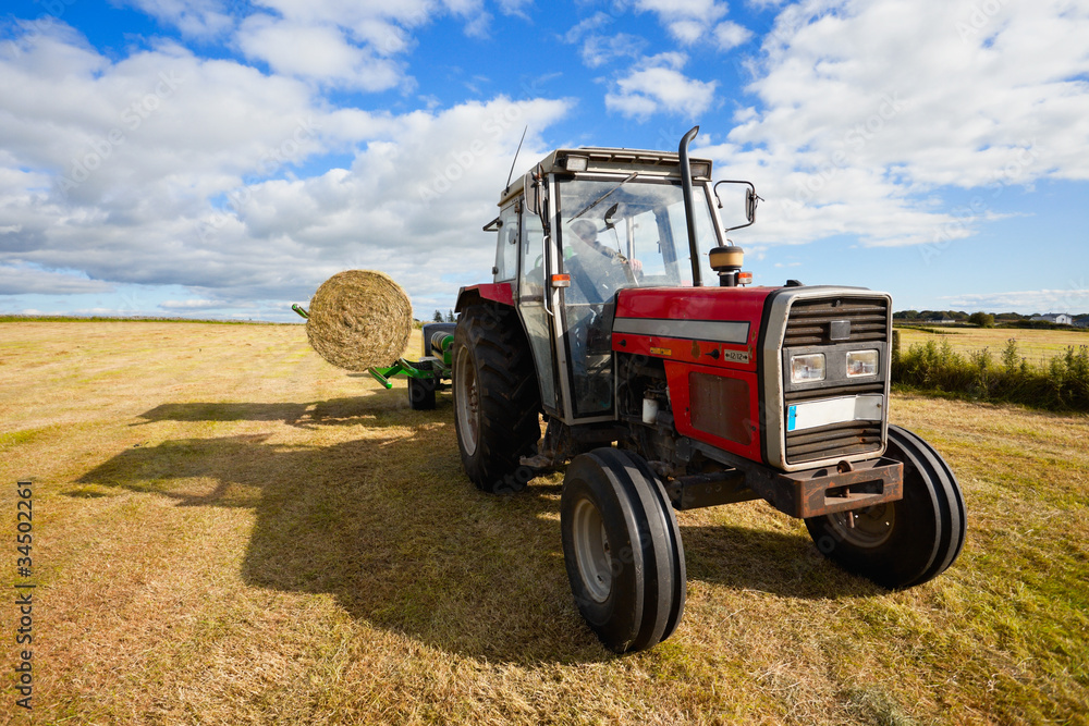 tractor collecting a roll of haystack in the field tractor collecting a roll of haystack in the field