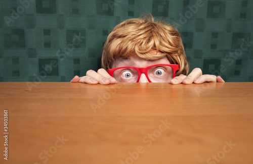 Scared nerd hiding behind a desk photo
