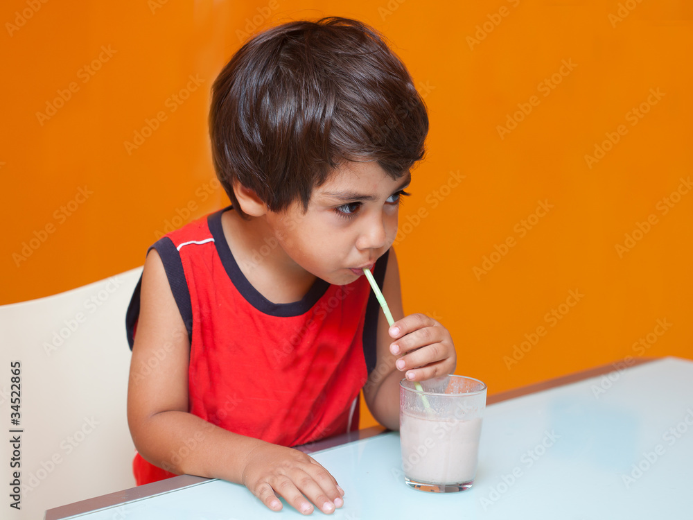 bambino beve latte dal bicchiere con la cannuccia Stock Photo