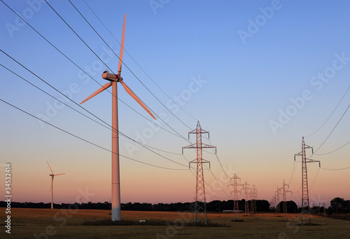 Quadro em tela Electricity pylons and wind turbines against sky at sunset