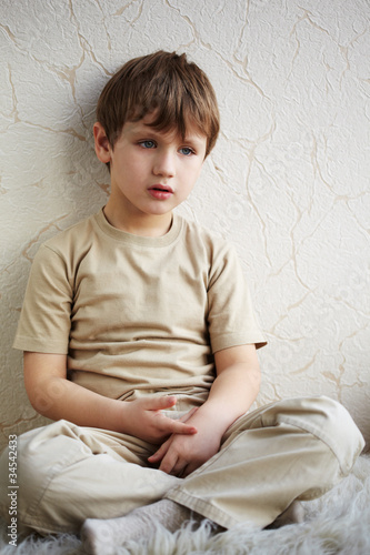 Bilde på lerret Little boy sits alone on a fleecy white rug