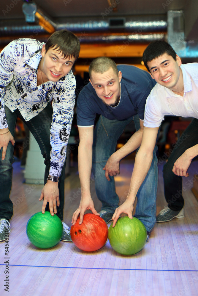 Fototapeta premium Three men bent over to heave up balls for bowling