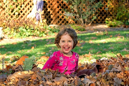 Young girl jumps into a pile of autumn leaves