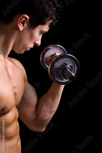 Muscular young man lifting dumbbells on black background.