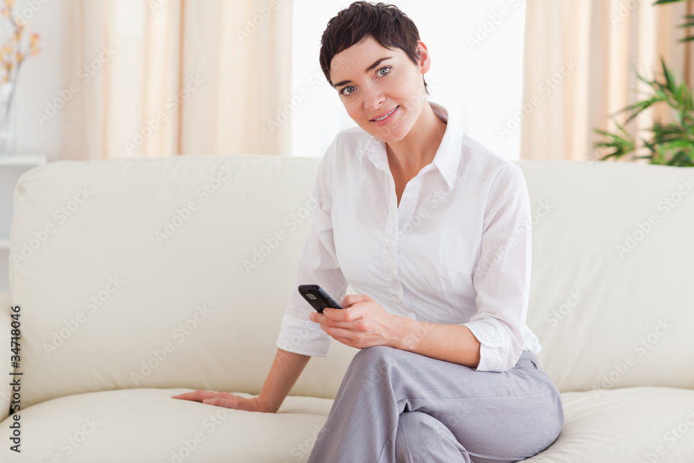 Smiling brunette Woman sitting on a sofa with a phone Smiling brunette Woman sitting on a sofa with a phone