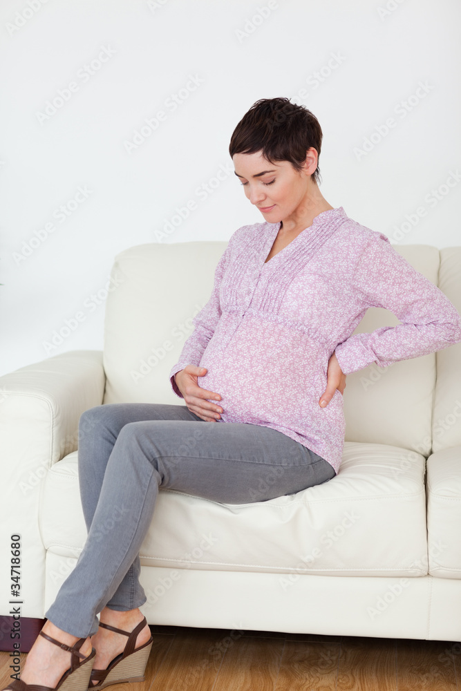 Pregnant woman sitting on a sofa touching her belly Pregnant woman sitting on a sofa touching her belly