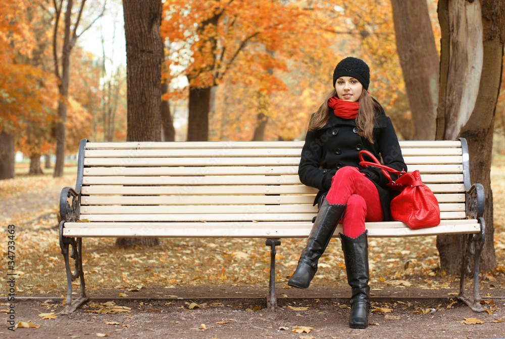 A young brunette woman sitting on a bench in a park