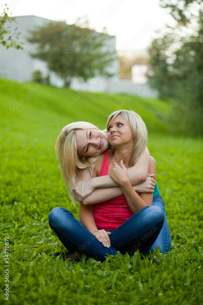 Fototapeta premium Two girls sitting on the grass, embracing