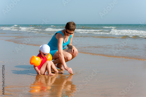 Billede på lærred Mother and baby are looking for shell