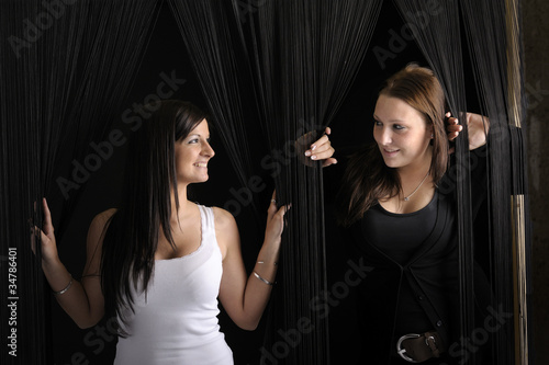 two young women looking from behind a cord curtain photo