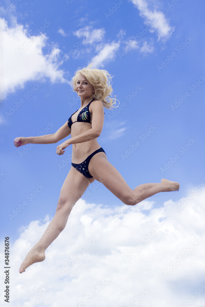 Young pretty girl in black swimsuit on jumps against blue sky Young pretty girl in black swimsuit on jumps against blue sky