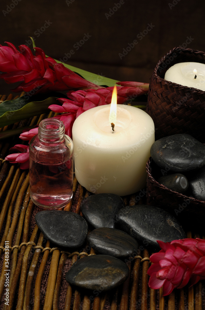 burning candle and pebble with ginger flower on bamboo mat