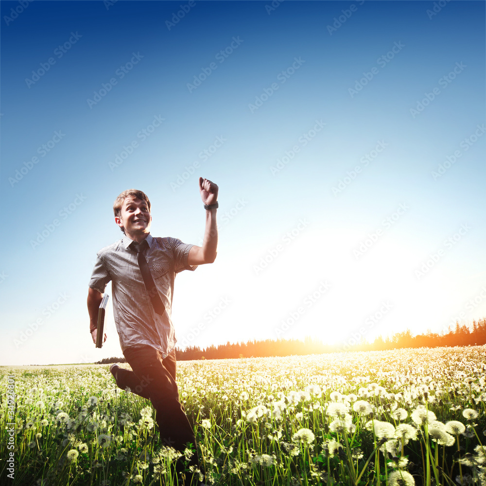 Happy young man with laptop in hand running on meadow with dandelions Happy young man with laptop in hand running on meadow with dandelions