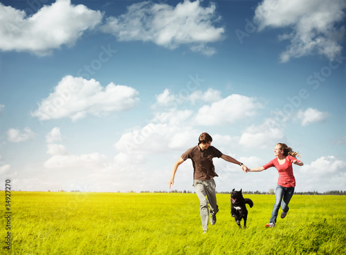 Young happy pair running on a green meadow with a dog