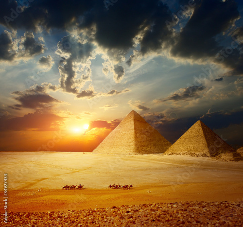 Grate pyramids in Giza valley in Egypt with a group of Bedouins on camels riding through the desert