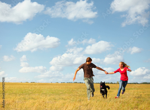 Young happy family running with dog on a green meadow