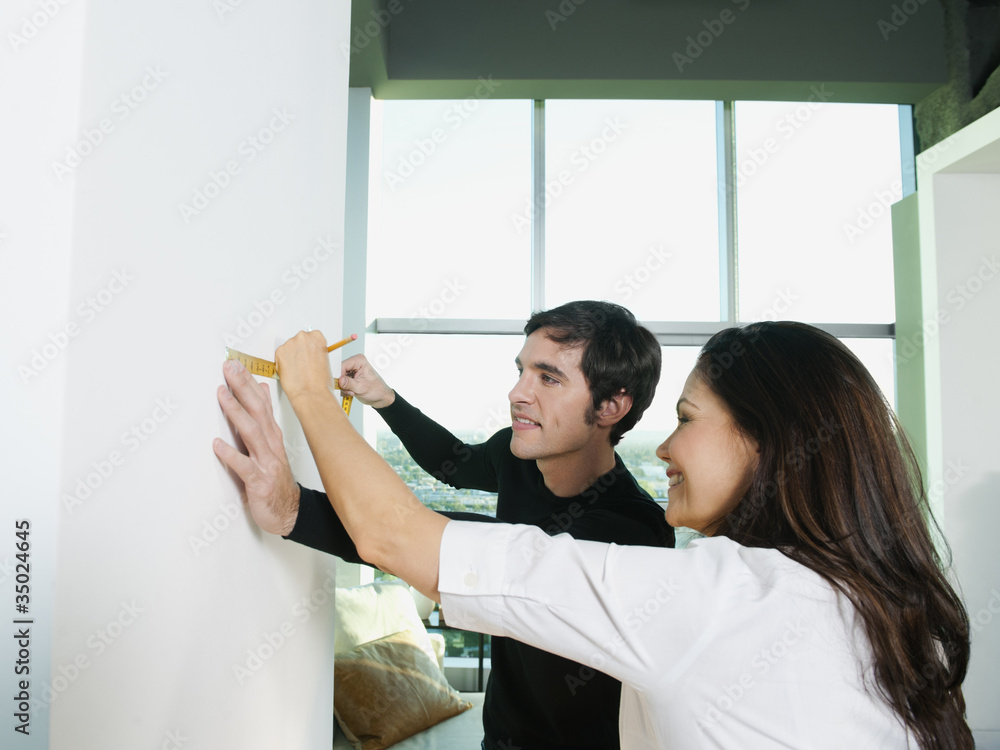 Couple marking wall with pencil and measuring tape Couple marking wall with pencil and measuring tape