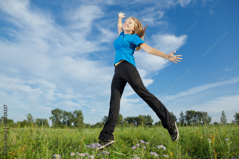 Happy girl jumps against a green grass and the blue sky