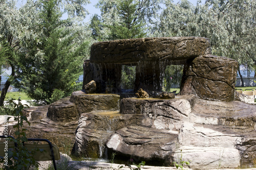 waterfall ove structure of stones in a park in front of trees